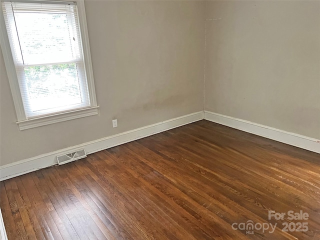 empty room featuring dark wood-style floors, baseboards, and visible vents