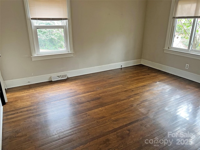 unfurnished room with visible vents, dark wood finished floors, and baseboards