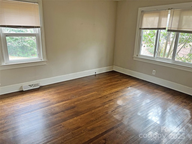 unfurnished room with baseboards, visible vents, dark wood-type flooring, and a wealth of natural light