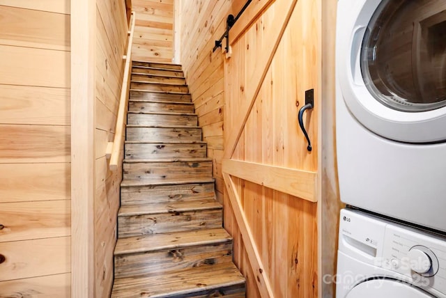 stairs with a barn door, stacked washer and dryer, and wooden walls