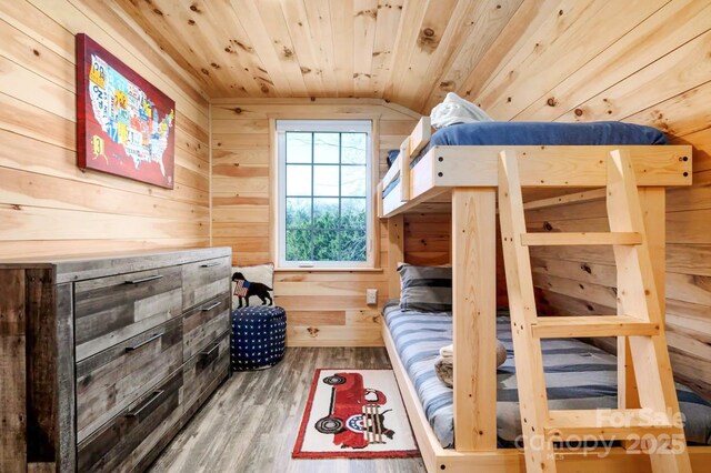 bedroom with vaulted ceiling, wooden walls, wood ceiling, and wood finished floors