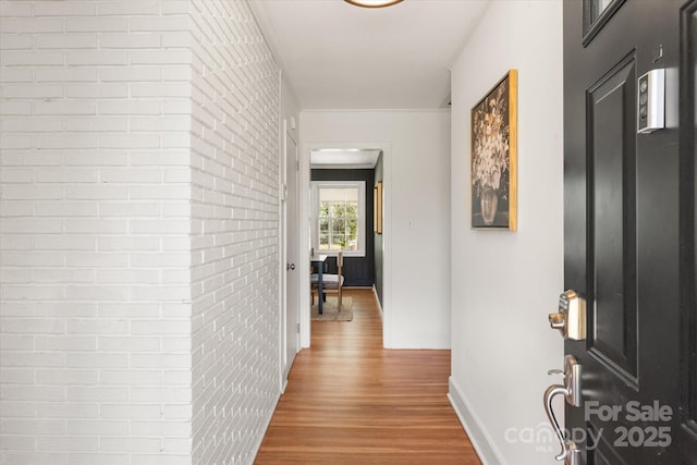 hallway with wood finished floors, baseboards, and brick wall