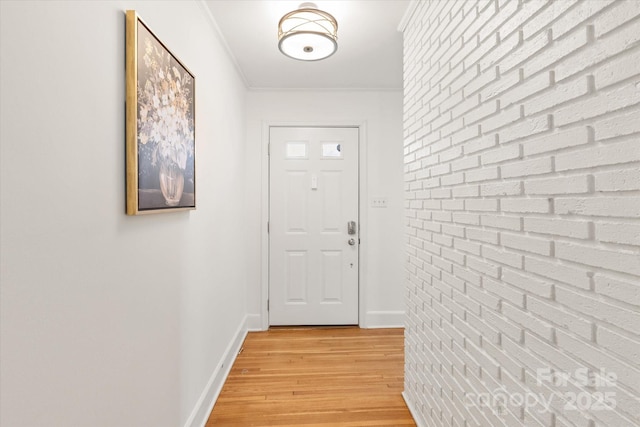 doorway to outside featuring crown molding, light wood finished floors, baseboards, and brick wall