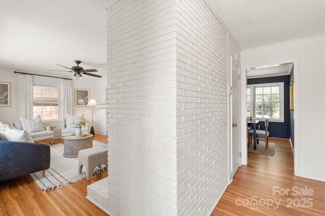 hall with baseboards, light wood-style floors, and brick wall