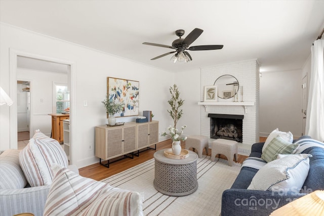 living room with a brick fireplace, a ceiling fan, and wood finished floors