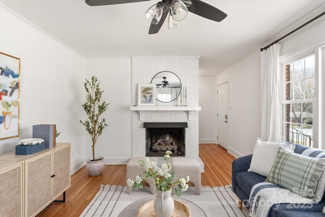 living room featuring a brick fireplace, wood finished floors, and crown molding