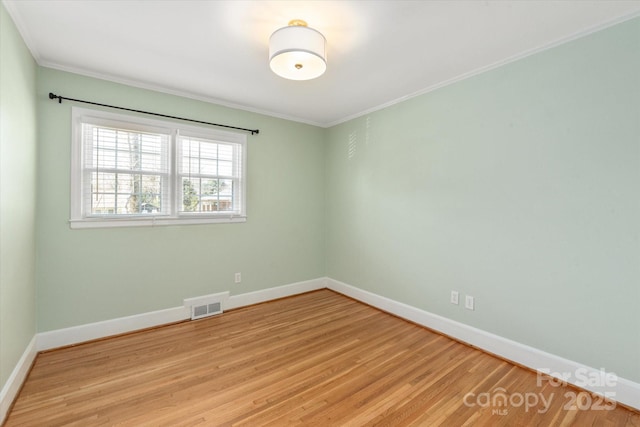 unfurnished room with light wood-type flooring, visible vents, baseboards, and ornamental molding