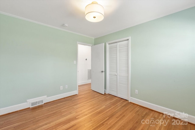 unfurnished bedroom featuring light wood-type flooring, visible vents, baseboards, and a closet