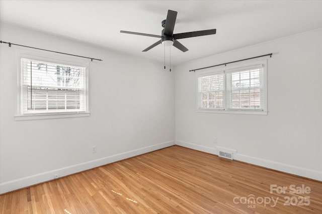 empty room with light wood-style floors, visible vents, a wealth of natural light, and baseboards