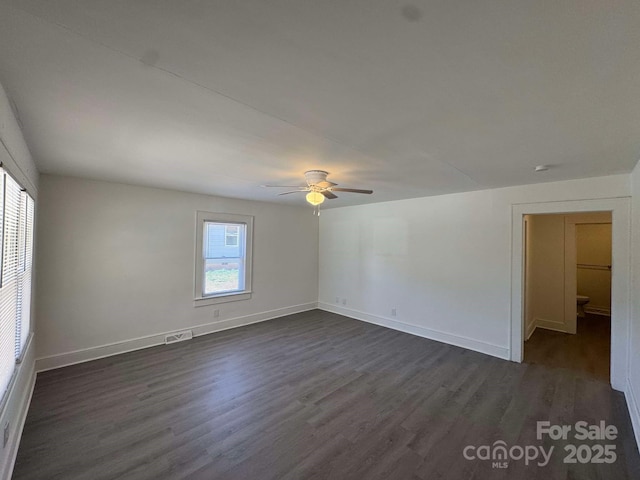 unfurnished room with dark wood-style floors, visible vents, ceiling fan, and baseboards