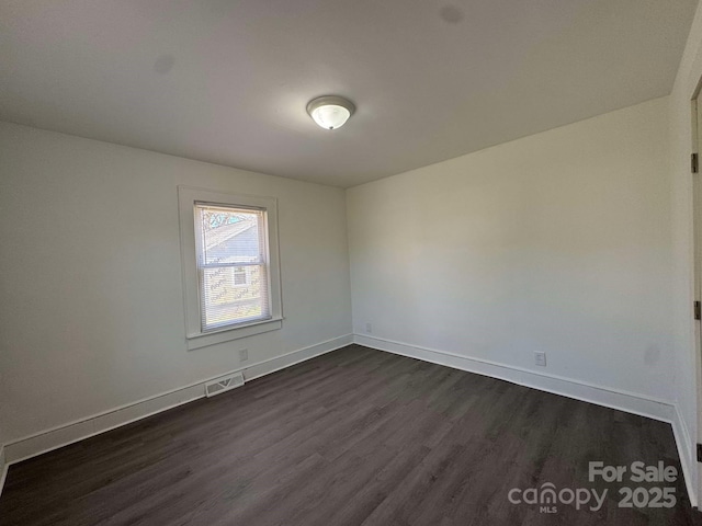 empty room featuring baseboards, visible vents, and dark wood-type flooring