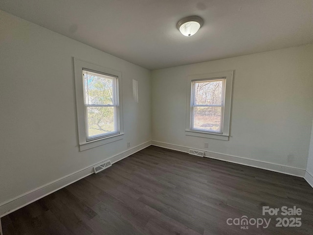 empty room featuring a healthy amount of sunlight, visible vents, and dark wood finished floors