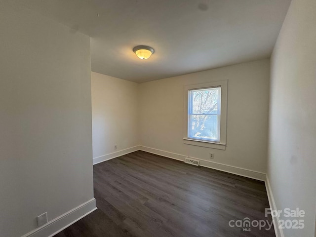 unfurnished room with dark wood-type flooring, visible vents, and baseboards