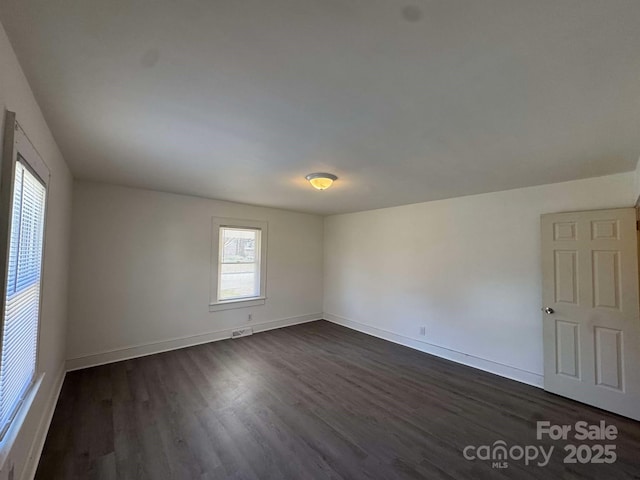 empty room with baseboards, visible vents, and dark wood finished floors