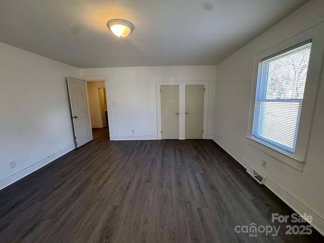 unfurnished bedroom with visible vents, dark wood finished floors, and baseboards