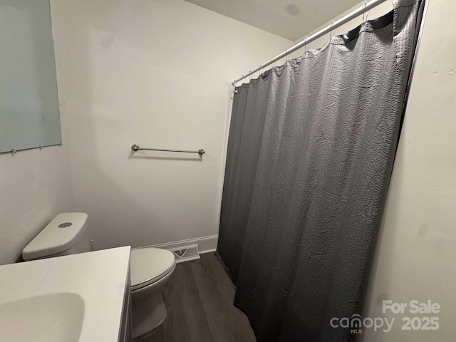 bathroom with curtained shower, toilet, vanity, wood finished floors, and baseboards