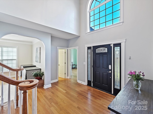 entrance foyer with arched walkways, stairway, a high ceiling, light wood-type flooring, and baseboards