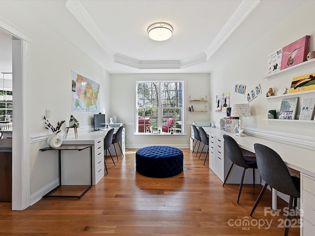 office area featuring baseboards, ornamental molding, a tray ceiling, light wood-type flooring, and built in desk