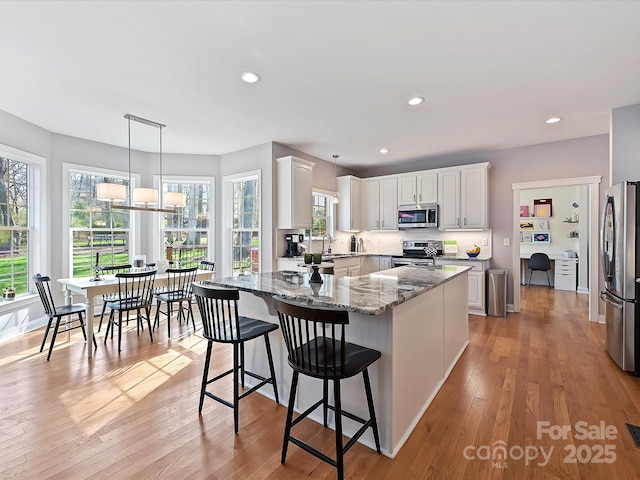 kitchen with recessed lighting, appliances with stainless steel finishes, light wood-style floors, white cabinets, and light stone countertops