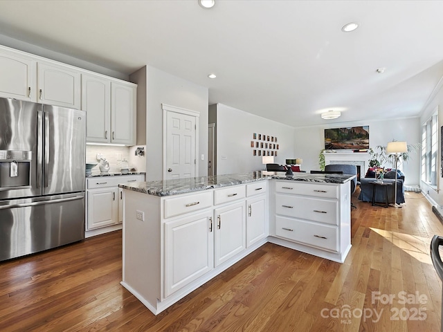 kitchen featuring white cabinets, dark stone countertops, dark wood-type flooring, a fireplace, and stainless steel refrigerator with ice dispenser