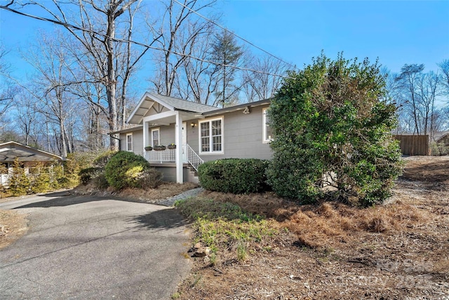 view of front facade featuring aphalt driveway, covered porch, and fence