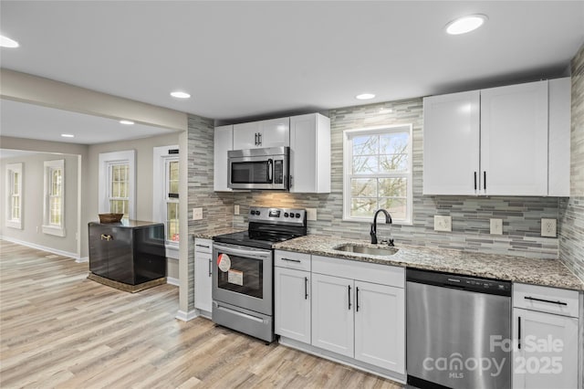 kitchen with a sink, light wood-style flooring, tasteful backsplash, and appliances with stainless steel finishes