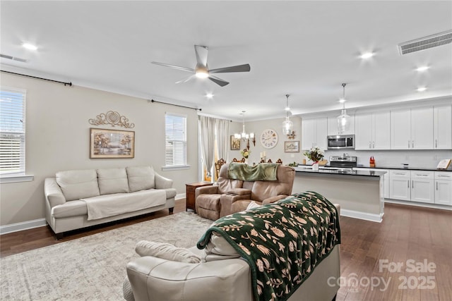 living room with dark wood-type flooring, ceiling fan with notable chandelier, visible vents, and baseboards