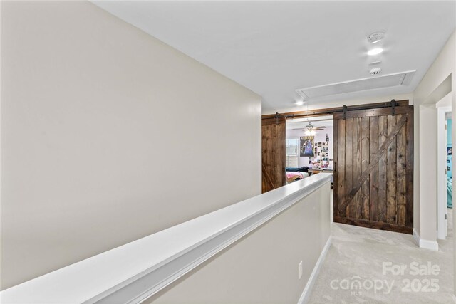 hall featuring a barn door, baseboards, attic access, and carpet flooring