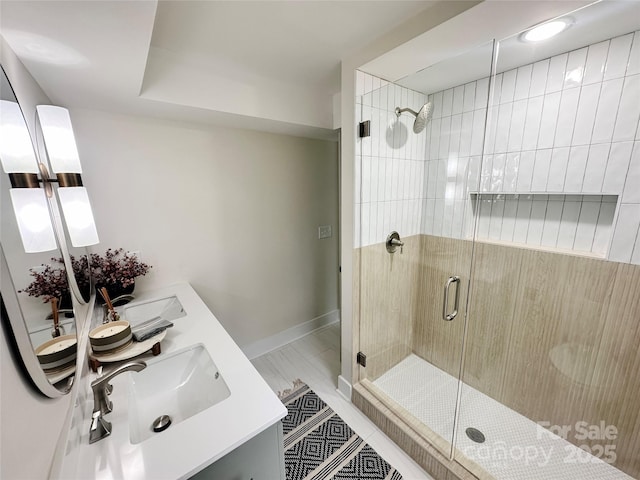 full bath featuring a stall shower, a sink, baseboards, and double vanity