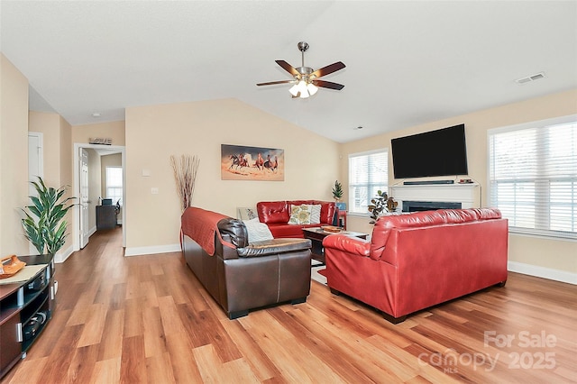 living room with visible vents, baseboards, lofted ceiling, light wood-style flooring, and a fireplace