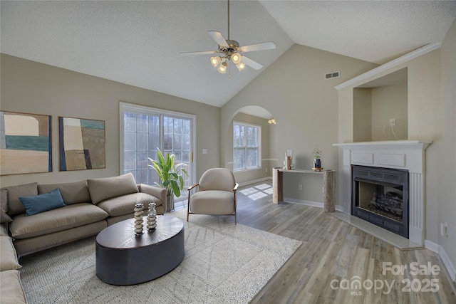 living room with arched walkways, a fireplace, visible vents, light wood-type flooring, and baseboards