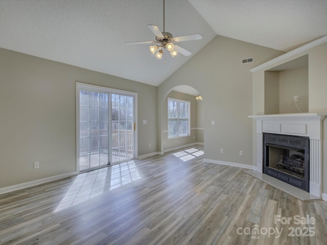 unfurnished living room featuring arched walkways, a fireplace, visible vents, and light wood-style floors