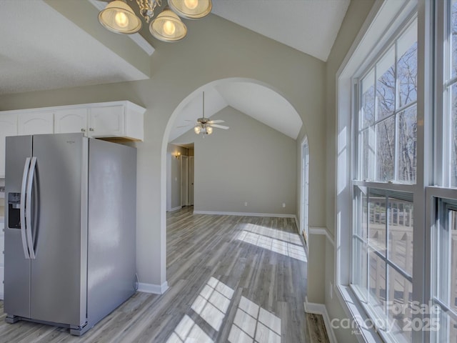 kitchen with arched walkways, stainless steel fridge, lofted ceiling, and white cabinetry