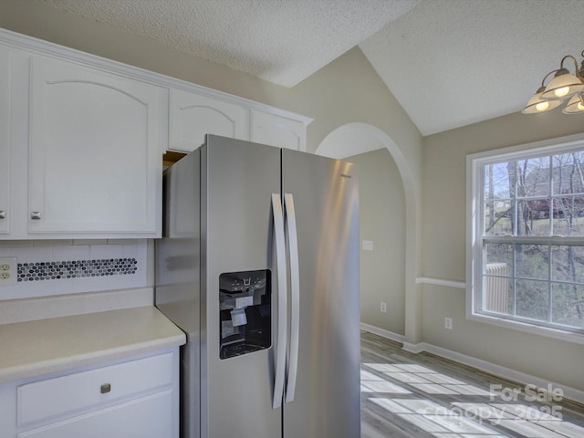 kitchen featuring arched walkways, light countertops, white cabinetry, a textured ceiling, and stainless steel fridge