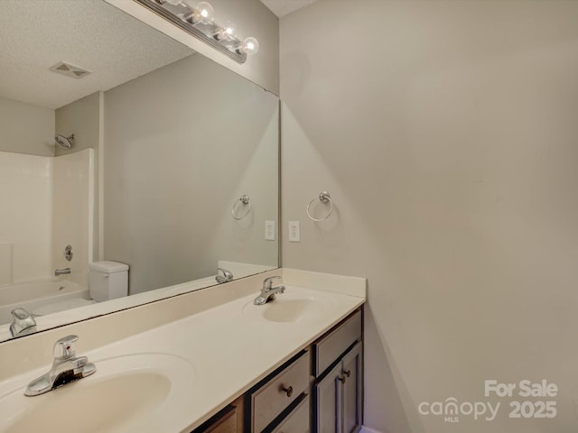 full bath featuring a textured ceiling, double vanity, a sink, and visible vents