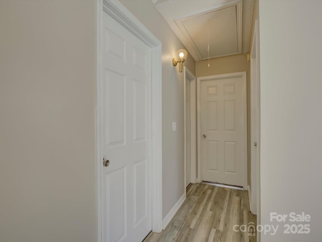 corridor featuring light wood-style floors, attic access, and baseboards