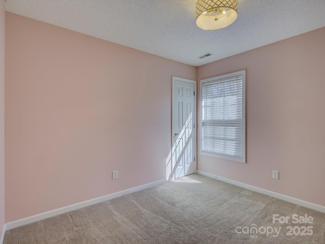 carpeted spare room featuring visible vents, a textured ceiling, and baseboards