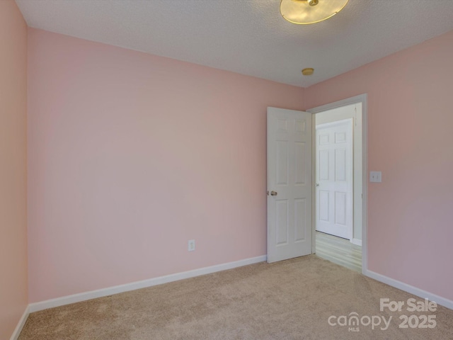 empty room with carpet, a textured ceiling, and baseboards