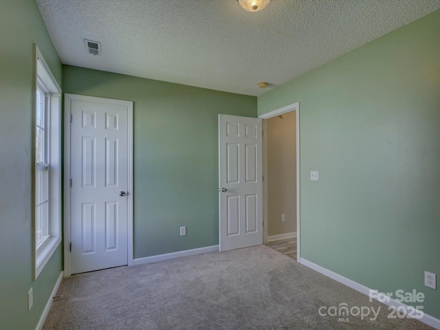 unfurnished bedroom featuring a textured ceiling, carpet flooring, visible vents, and baseboards