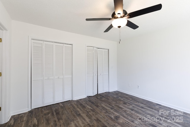 unfurnished bedroom with baseboards, ceiling fan, dark wood-style flooring, a textured ceiling, and two closets