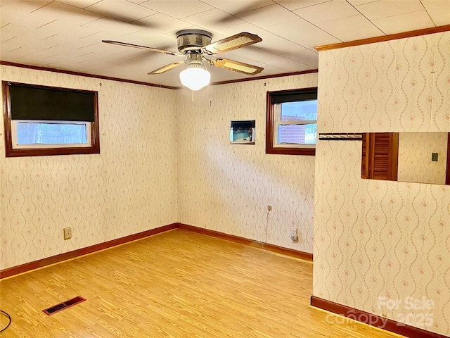 unfurnished room featuring wallpapered walls, light wood-style flooring, visible vents, and crown molding