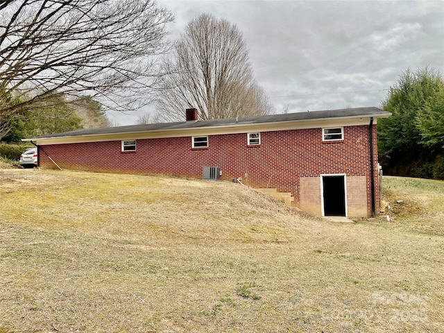 rear view of property with central air condition unit, a yard, a chimney, and brick siding