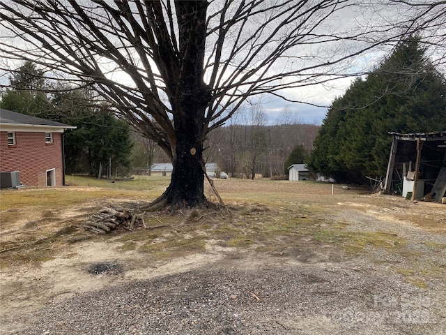 view of yard with cooling unit, a view of trees, and an outbuilding