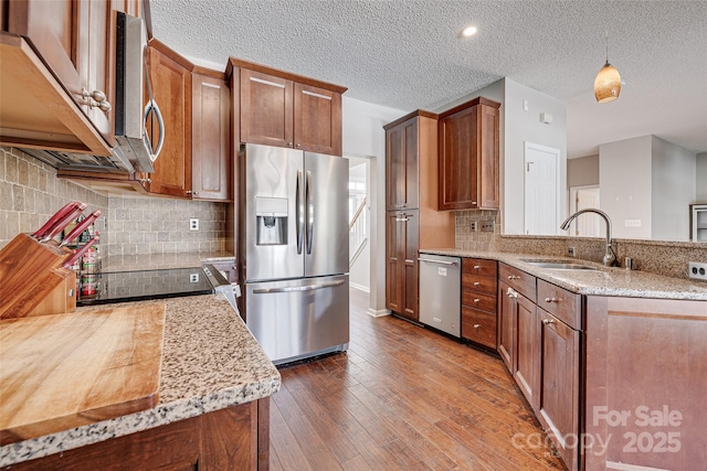 kitchen with dark wood finished floors, appliances with stainless steel finishes, a sink, light stone countertops, and a peninsula