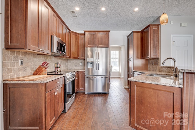 kitchen with stainless steel appliances, dark wood-type flooring, a sink, light stone countertops, and a peninsula