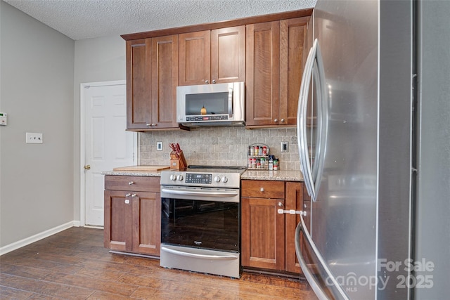 kitchen with baseboards, brown cabinetry, dark wood-type flooring, stainless steel appliances, and backsplash