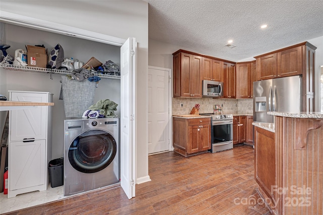 kitchen with appliances with stainless steel finishes, washer / clothes dryer, brown cabinetry, and light wood-style floors