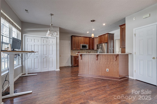 kitchen with appliances with stainless steel finishes, a breakfast bar, dark wood-type flooring, a peninsula, and hanging light fixtures