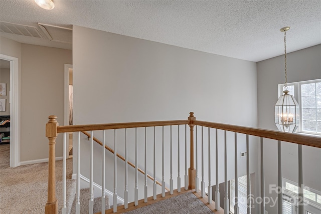 hall with a textured ceiling, carpet flooring, an upstairs landing, visible vents, and baseboards