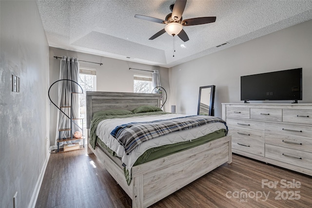 bedroom with a raised ceiling, visible vents, dark wood finished floors, and a textured ceiling